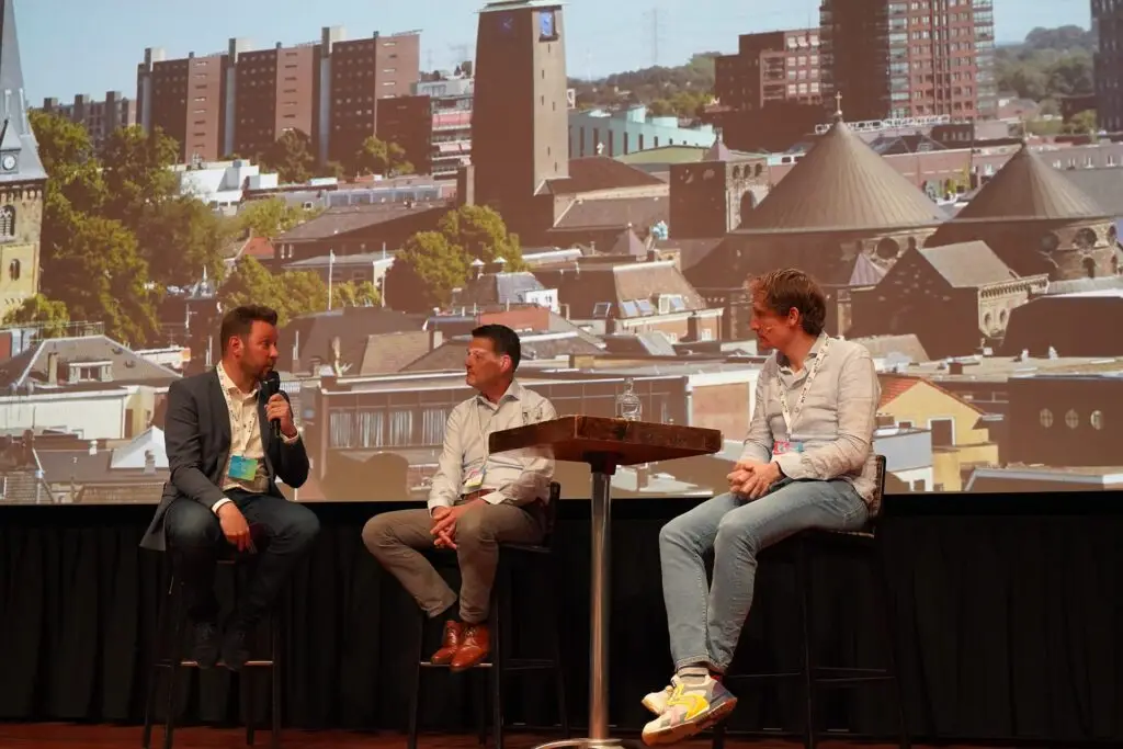 drie personen zittend op krukken op een podium in een interview