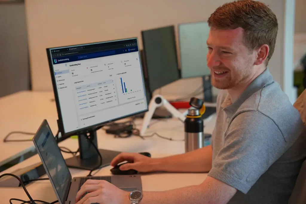 Glimlachende medewerker werkt achter een beeldscherm met het dashboard van Corsa Zaakbehandeling