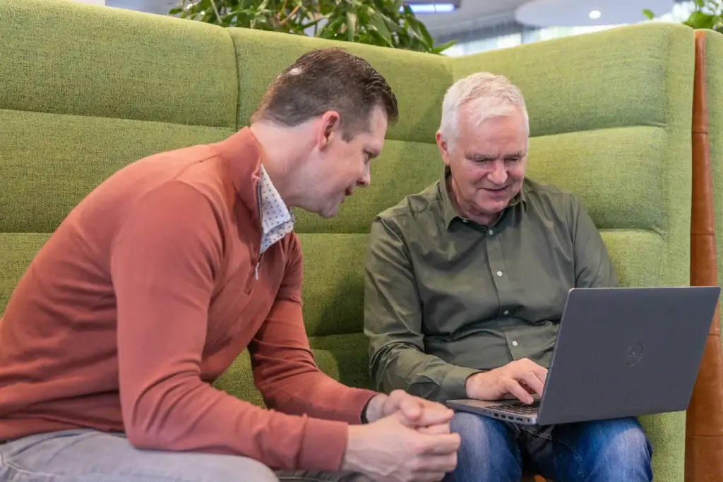 Twee collega's bekijken samen een laptop op een groene zitbank