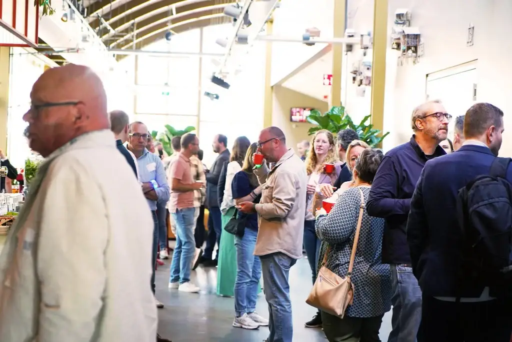 Bezoekers netwerken met een drankje tijdens het C the Next Step event in een lichte industriële eventlocatie.