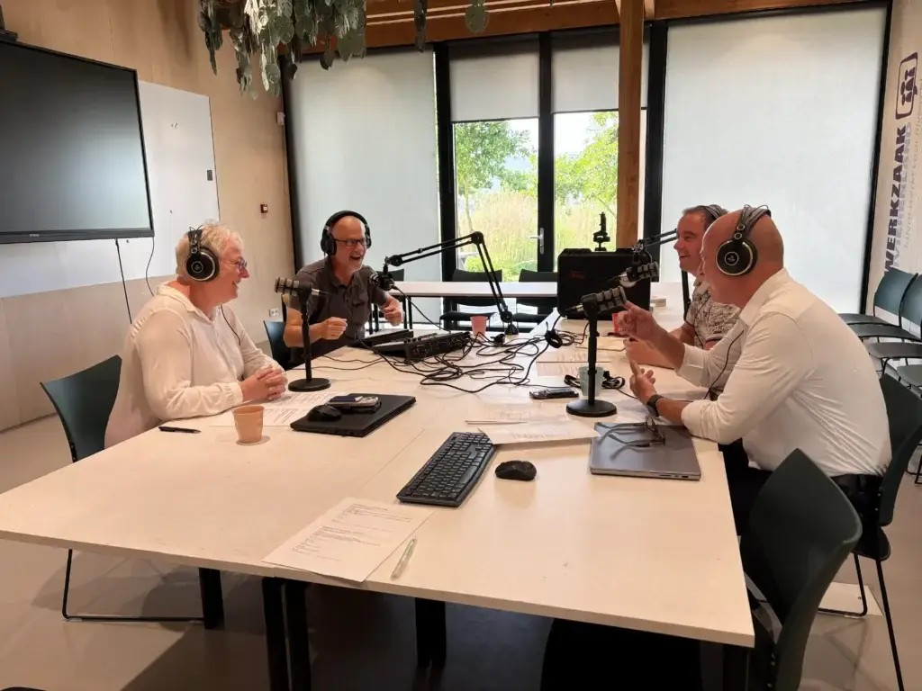 Vier deelnemers met koptelefoons nemen een podcast op rond een tafel met microfoons bij Werkzaak Rivierenland.